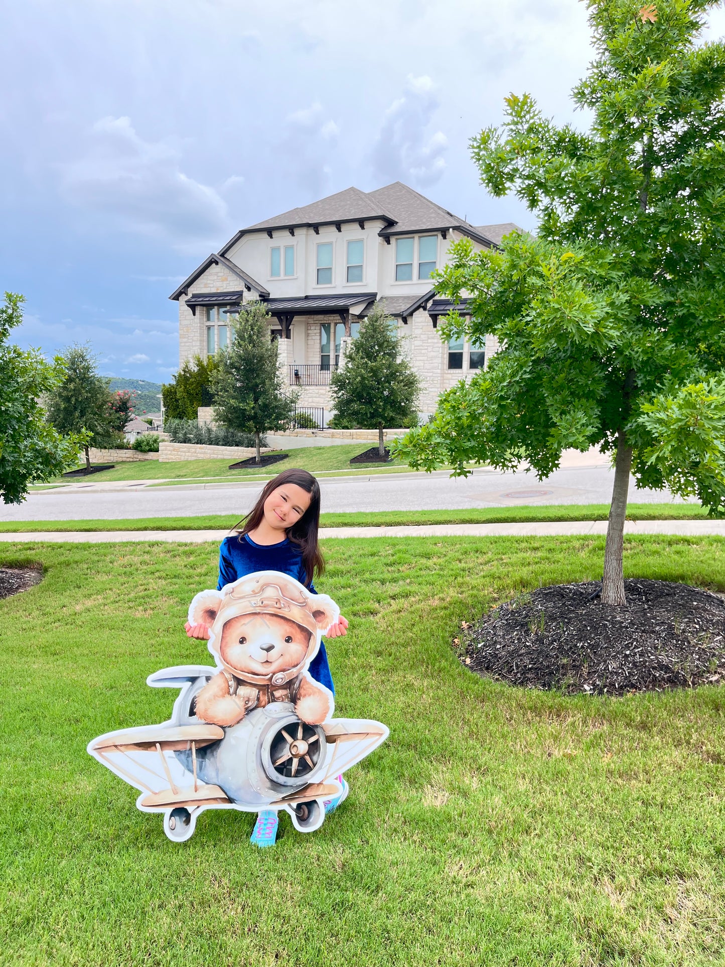 Person standing next to a decorative bear on a grassy lawn with a large house in the background. event decor character props cutout life size