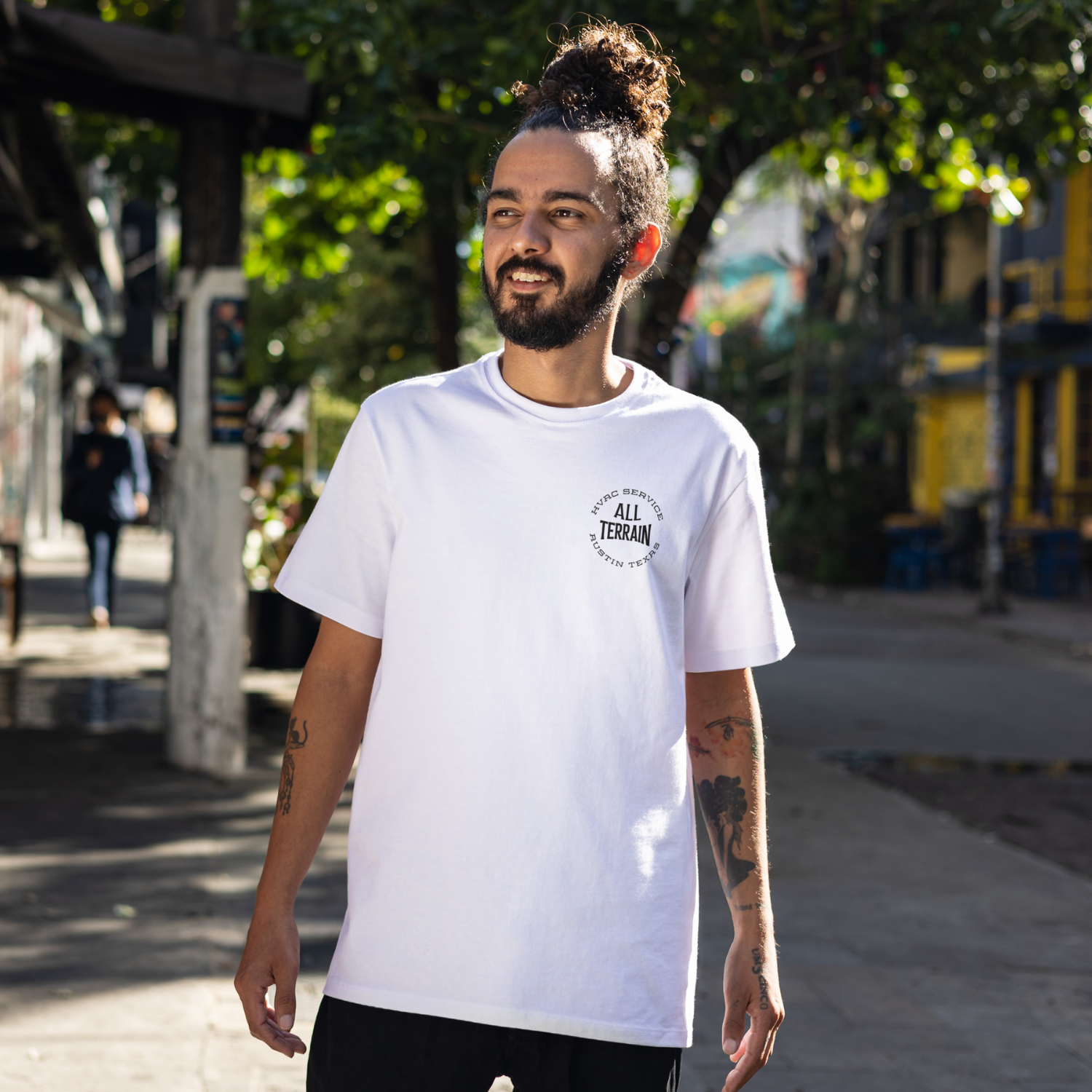 Man wearing a white t-shirt with 'All Terrain' logo outdoors. Person wearing a white t-shirt with text and a graphic on the back, standing on a city street. Funny tshirt, fun t shirt, when the ladies get hot, when the ladies got hot, they call me, all terrain HVAC jokes, HVAC contractor shirts