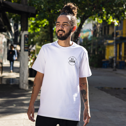 Man wearing a white t-shirt with 'All Terrain' logo outdoors. Person wearing a white t-shirt with text and a graphic on the back, standing on a city street. Funny tshirt, fun t shirt, when the ladies get hot, when the ladies got hot, they call me, all terrain HVAC jokes, HVAC contractor shirts