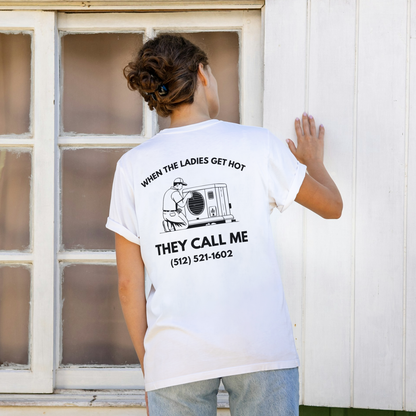 Women Person wearing a white t-shirt with text and phone number on the back, standing in front of a window. Person wearing a white t-shirt with text and a graphic on the back, standing on a city street. Funny tshirt, fun t shirt, when the ladies get hot, when the ladies got hot, they call me, all terrain HVAC jokes, HVAC contractor shirts