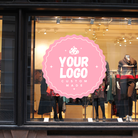 A pink window film with a custom logo placed on a store's display window, showcasing clothing items behind it.